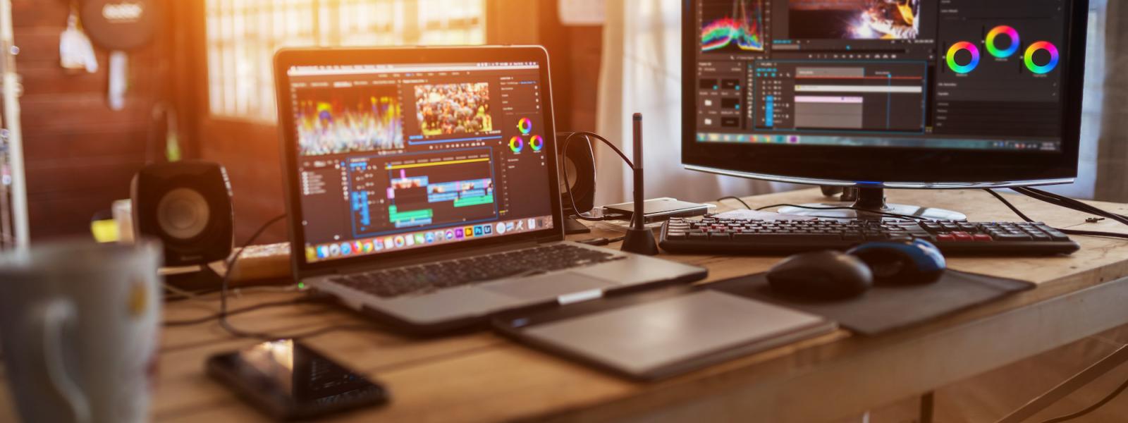 Laptop and external monitor on wooden desk with Adobe programs on screens