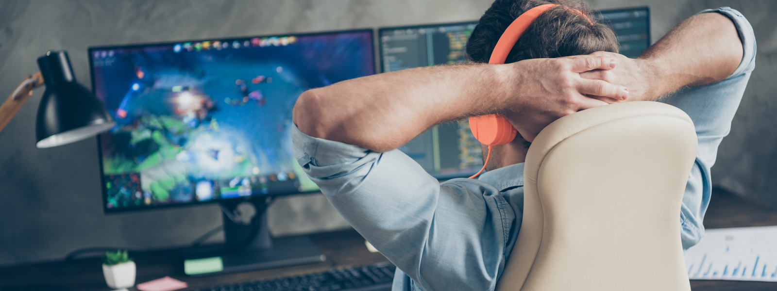 Man sitting in chair at desk with hands behind head looking at two monitors