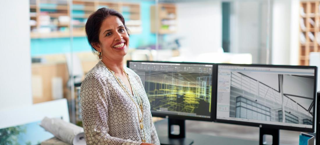 A woman sitting on a desktop workstation smiling into a camera 