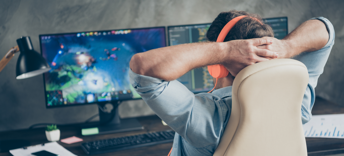 Man sitting in chair at desk with hands behind head looking at two monitors